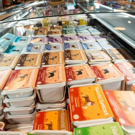 A refrigerated display case filled with various brands and flavors of packaged dog food, neatly stacked and organized.